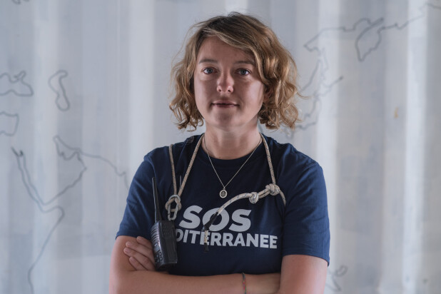 A white woman with wavy blonde hair wearing a navy blue t-shirt with a stethoscope around her neck