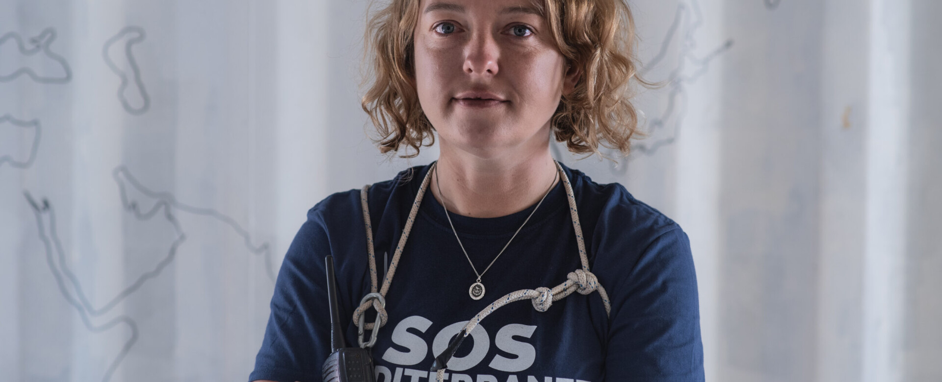 A white woman with wavy blonde hair wearing a navy blue t-shirt with a stethoscope around her neck