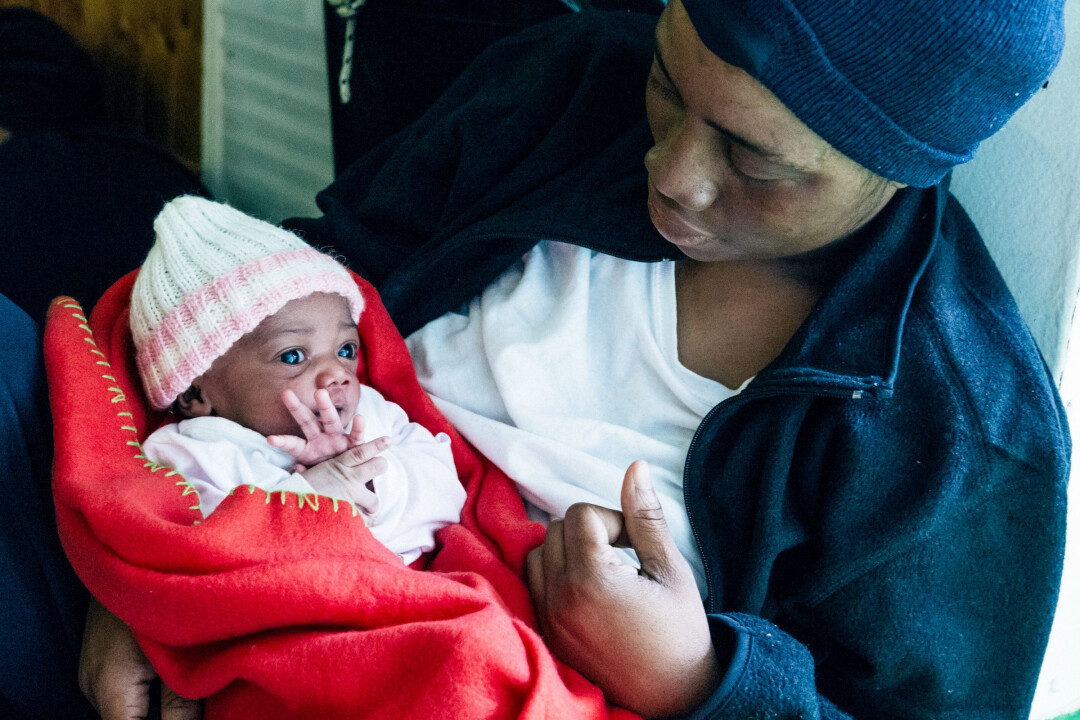a dark-skinned newborn baby wearing a knit hat, wrapped in a red blanket and being held by its moth
