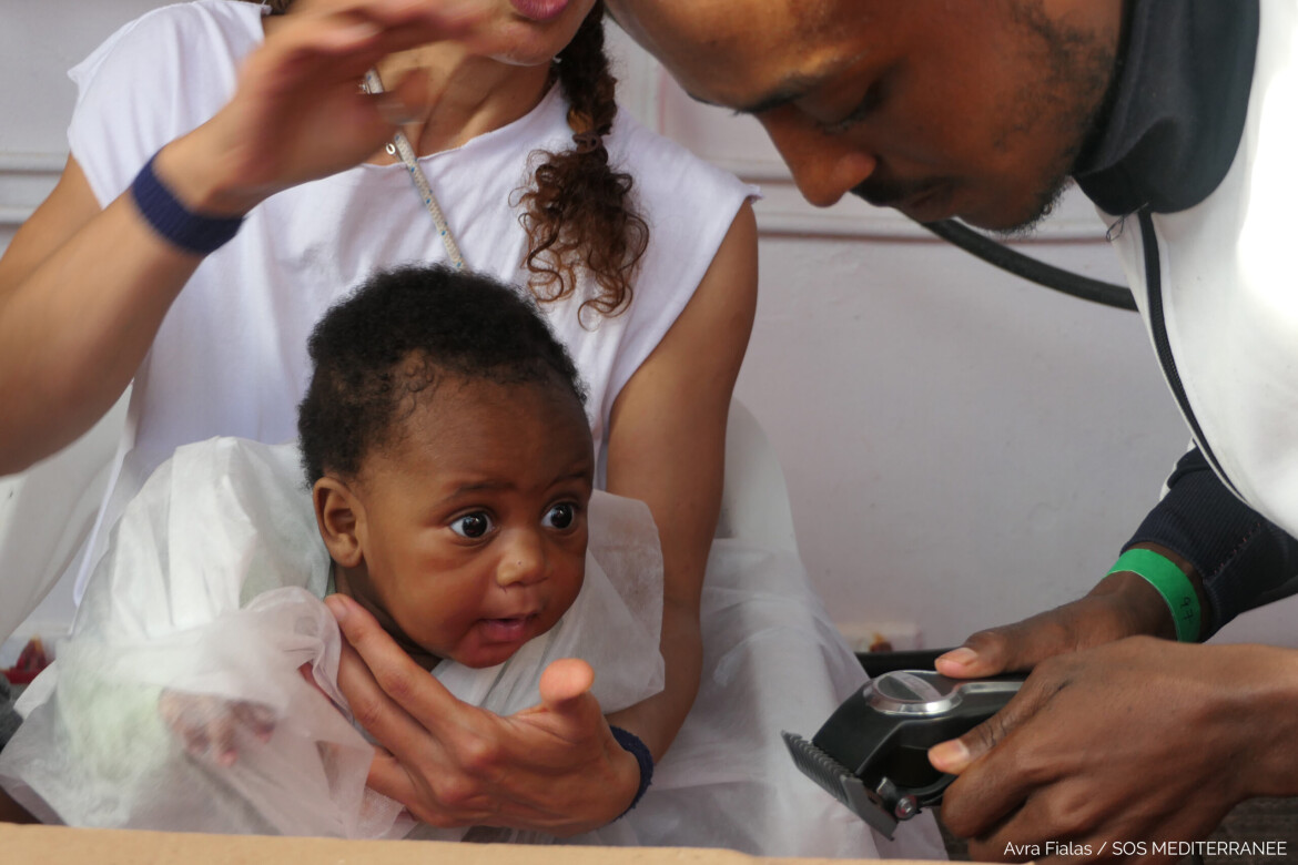 A black baby in the arms of a woman, with a man looking on