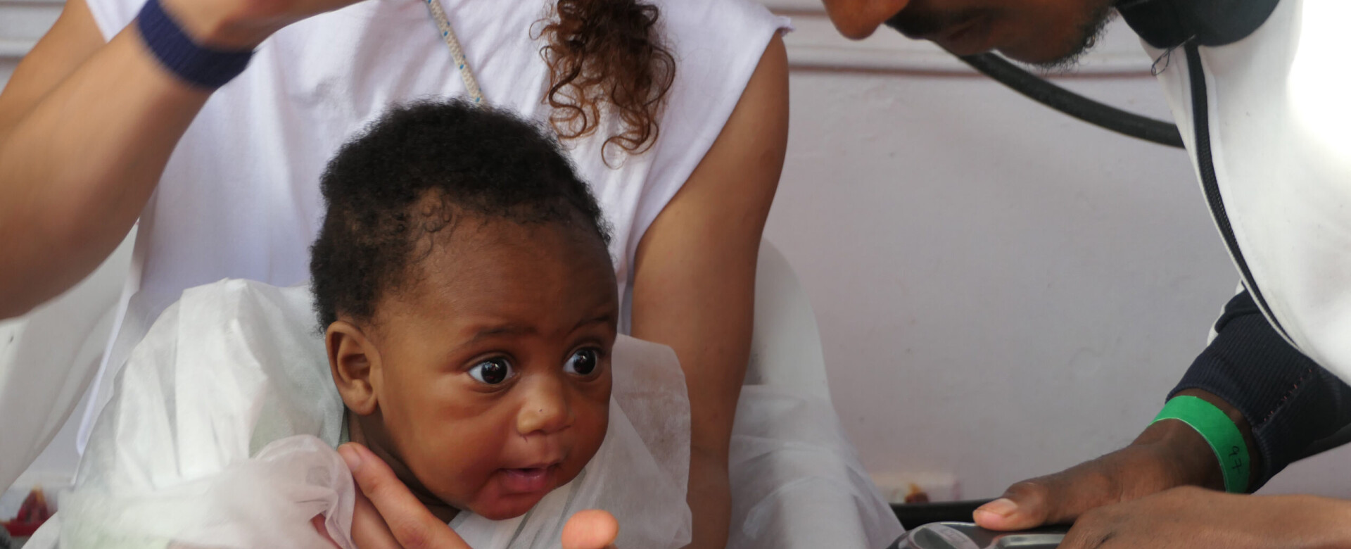 A black baby in the arms of a woman, with a man looking on