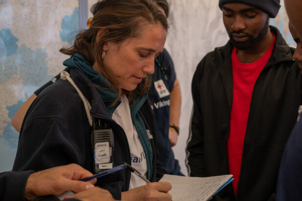 A humanitarian worker writes on a clipboard while speaking with people during a rescue operation.