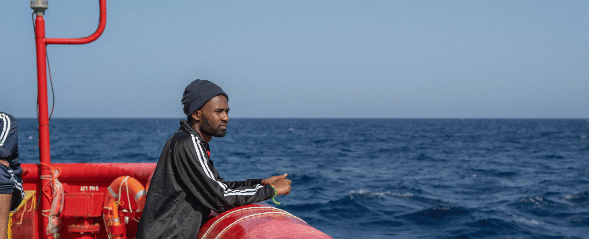 A man stands at the edge of a ship, looking out over the open sea on a clear day.