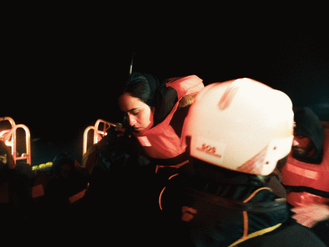 A rescue team assists a woman in a life jacket during a nighttime operation at sea.