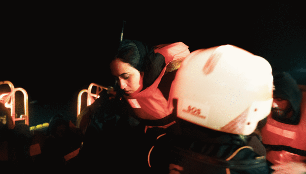 A rescue team assists a woman in a life jacket during a nighttime operation at sea.