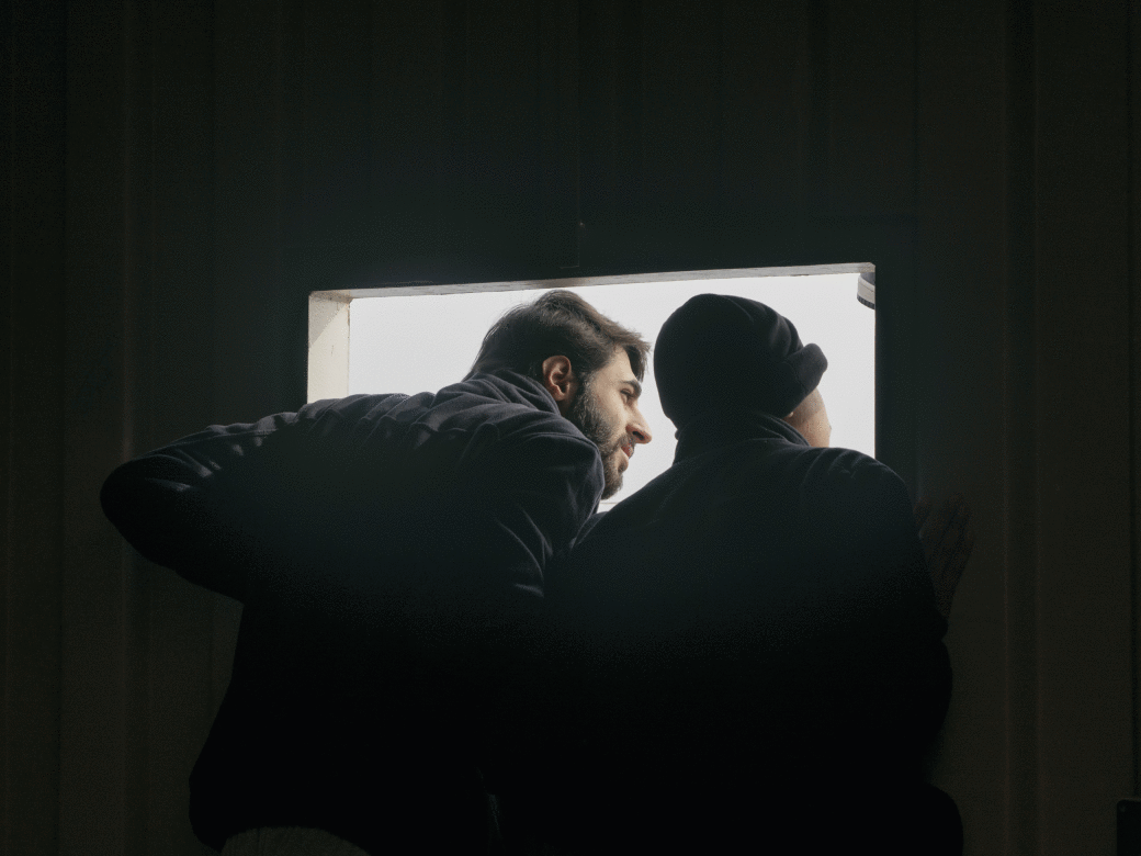 Two people lean through a window-like opening on a ship, looking outside toward the light.