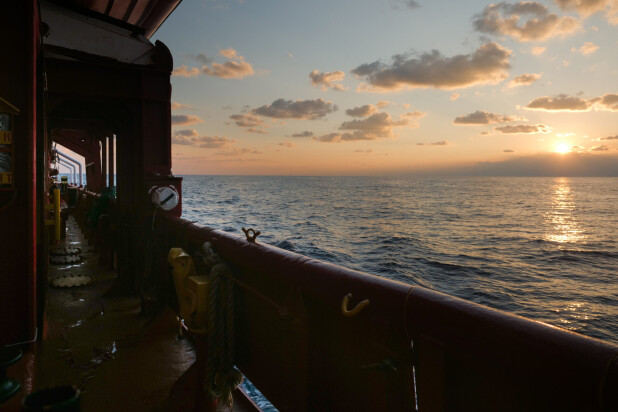 View of the ocean at sunset from a ship’s deck, with golden light reflecting off the water and rail