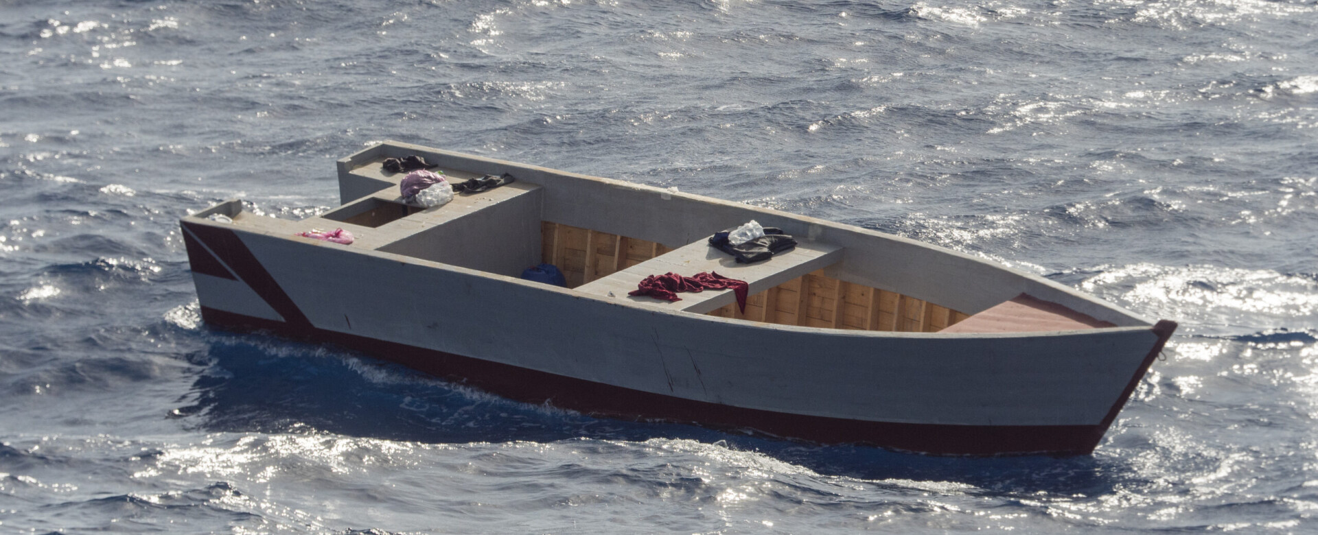 Empty wooden boat adrift in open sea under bright daylight.
