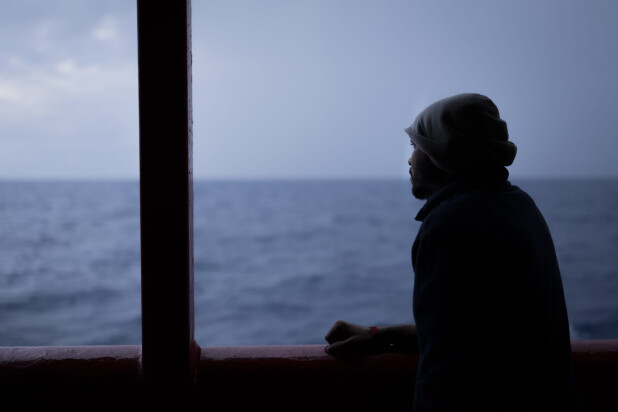 Silhouette of a person leaning on a ship’s railing, gazing out at the sea during dusk.
