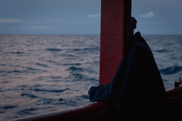 Silhouette of a person leaning on a ship’s railing, gazing out at the sea during dusk.