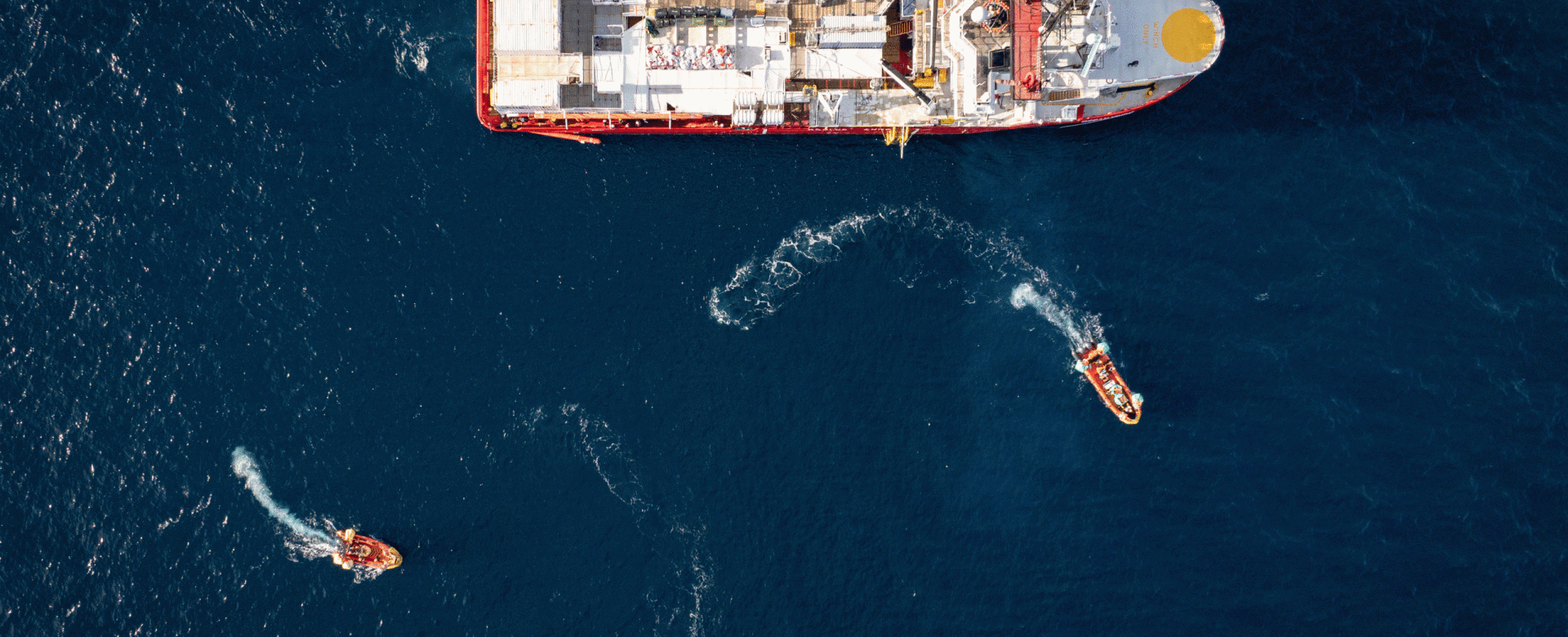 Aerial view of a rescue ship at sea with four small boats approaching it in curved paths across dee
